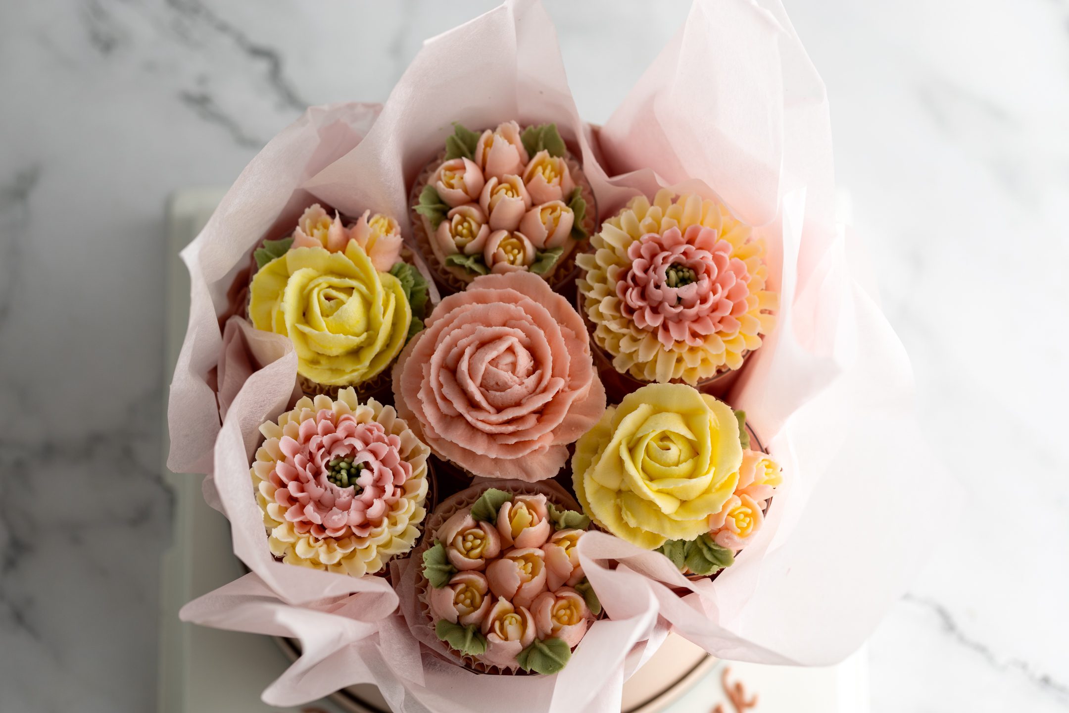 Sucré Cupcake Bouquet — floral cupcakes arranged in a pink round flower box inside crystal-clear gifting box with grosgrain ribbon