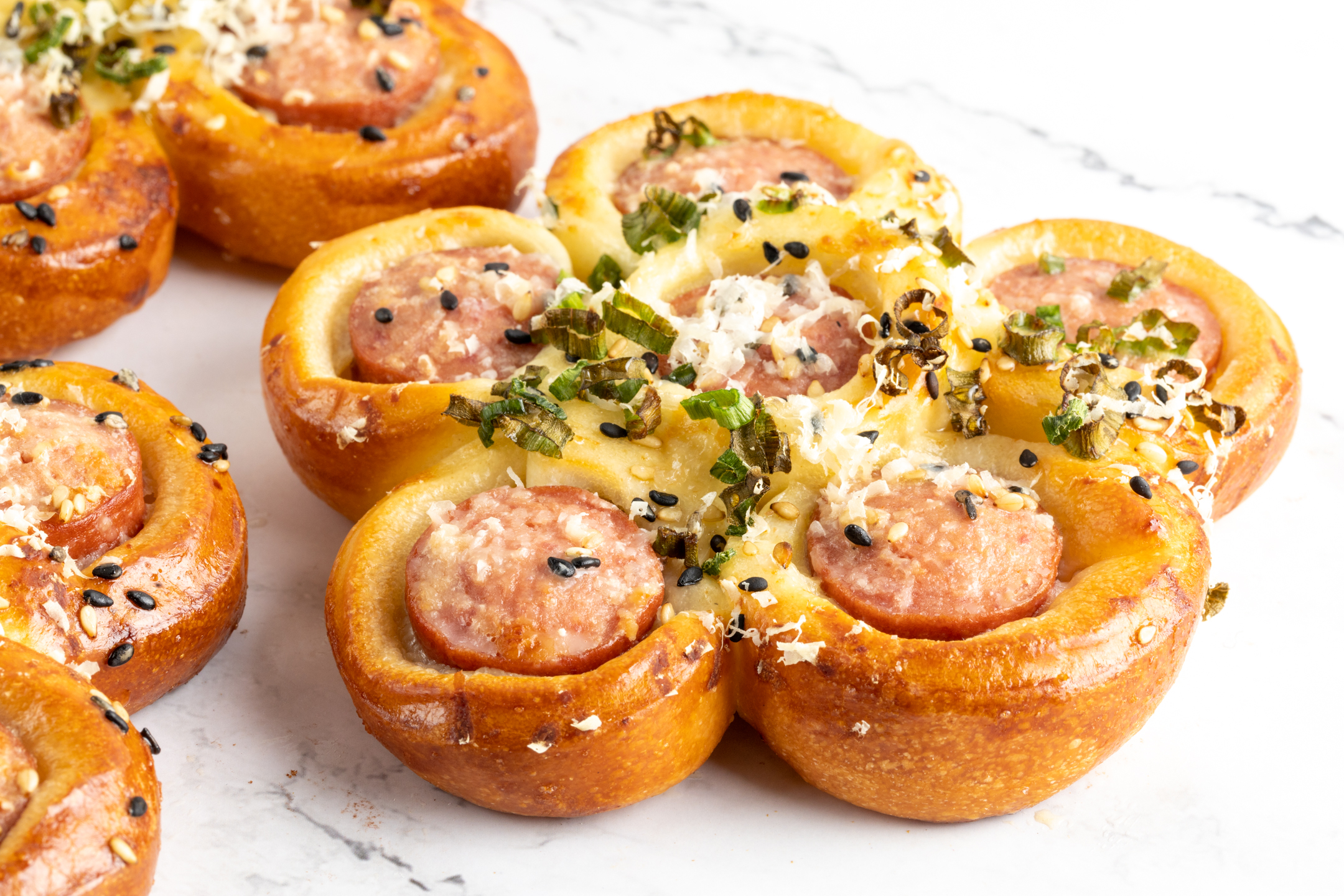 Hot Dog Flower Bun top view showing petal shape with sesame seeds, Parmigiano and green onion garnish