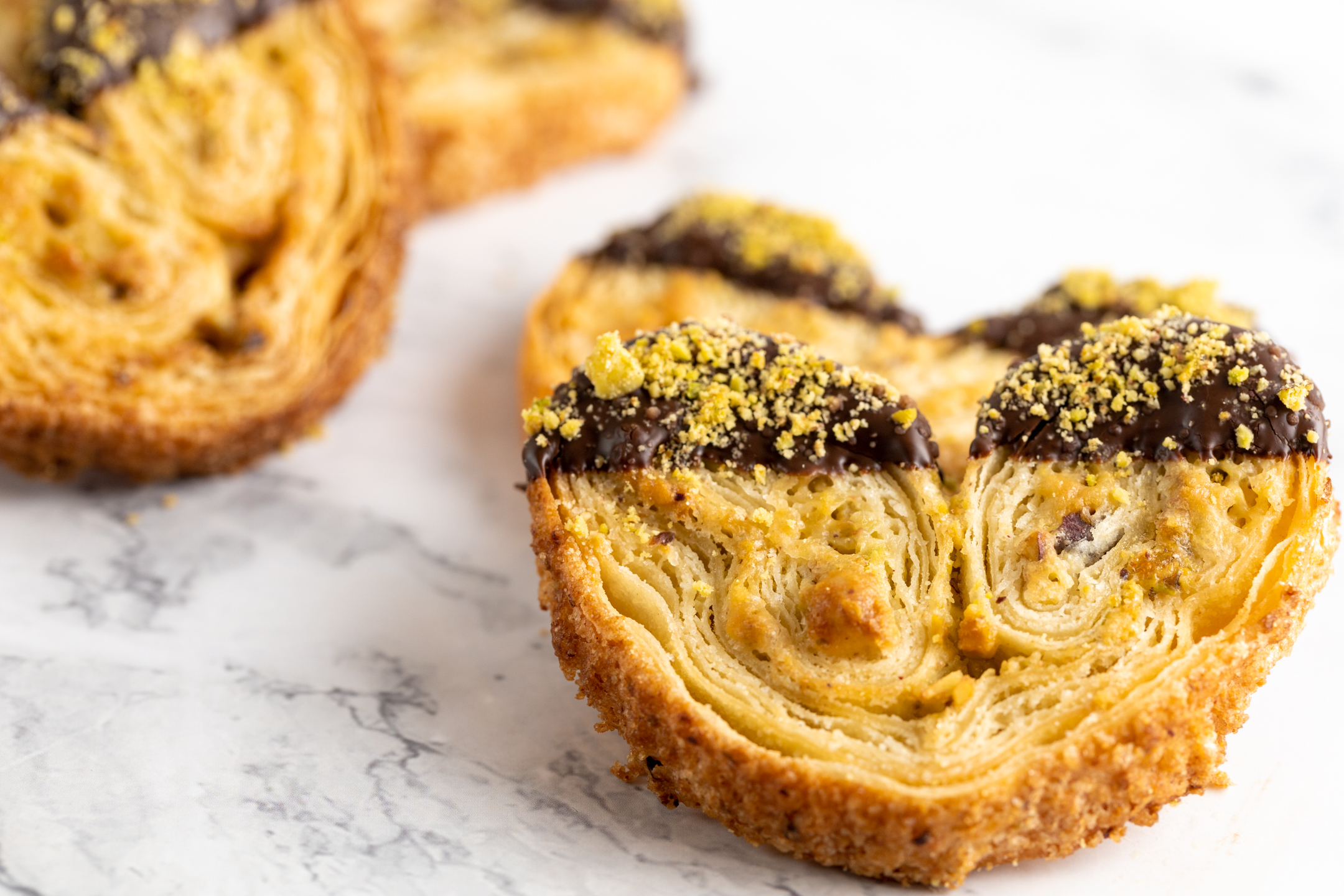 French Palmier close-up showing crispy laminated layers with pistachio and dark chocolate coating
