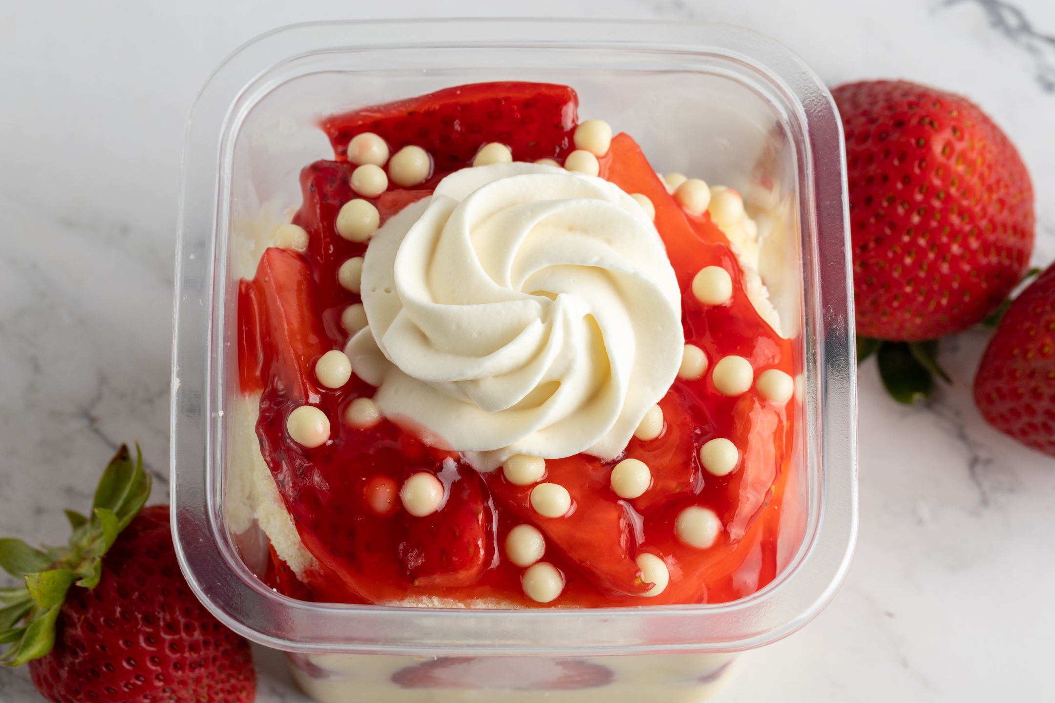 Fraisier in takeout container showing Chantilly cream swirl and chocolate pearl crisps