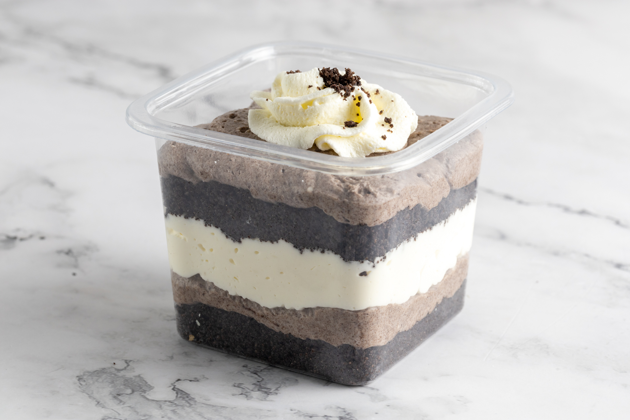 Oreo Cheesecake by Sucré in 12 oz to-go format — layered cheesecake with Oreo filling and Chantilly cream